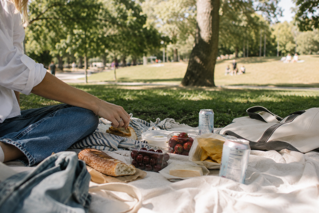 Simple grocery-store picnic with bread, fruit and cold drinks in a leafy local park on a late-summer afternoon.