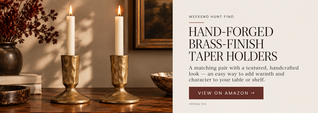 A matching pair of short textured brass-tone taper candle holders with ivory candles on a dark wood table.
