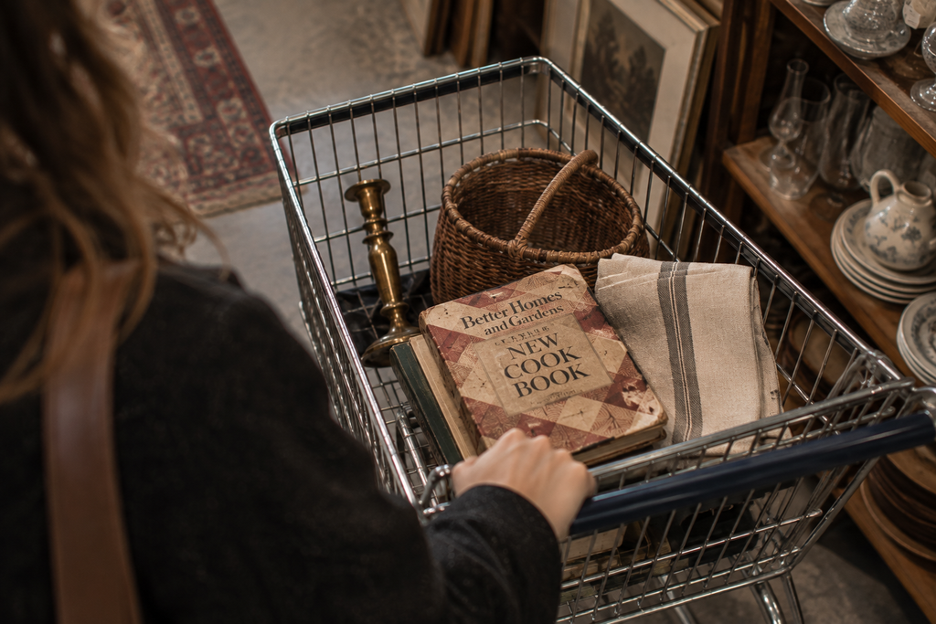Thrift store cart holding a cookbook, brass candlestick, linen and woven basket.
