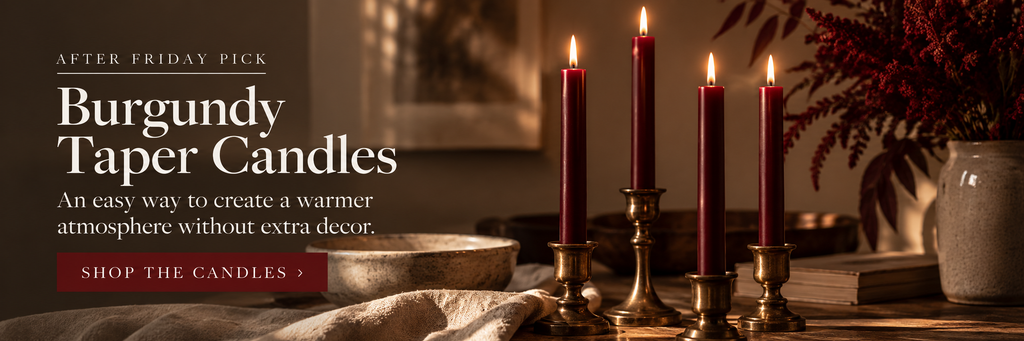 Burgundy taper candles burning in brass holders on a warm fall dinner table.